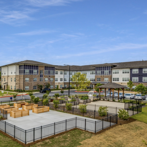 Exterior view of the Anthem at Riverside featuring landscaped outdoor spaces, picnic areas, and raised garden beds, with the residential building in the background showcasing a blend of modern and traditional architectural styles.